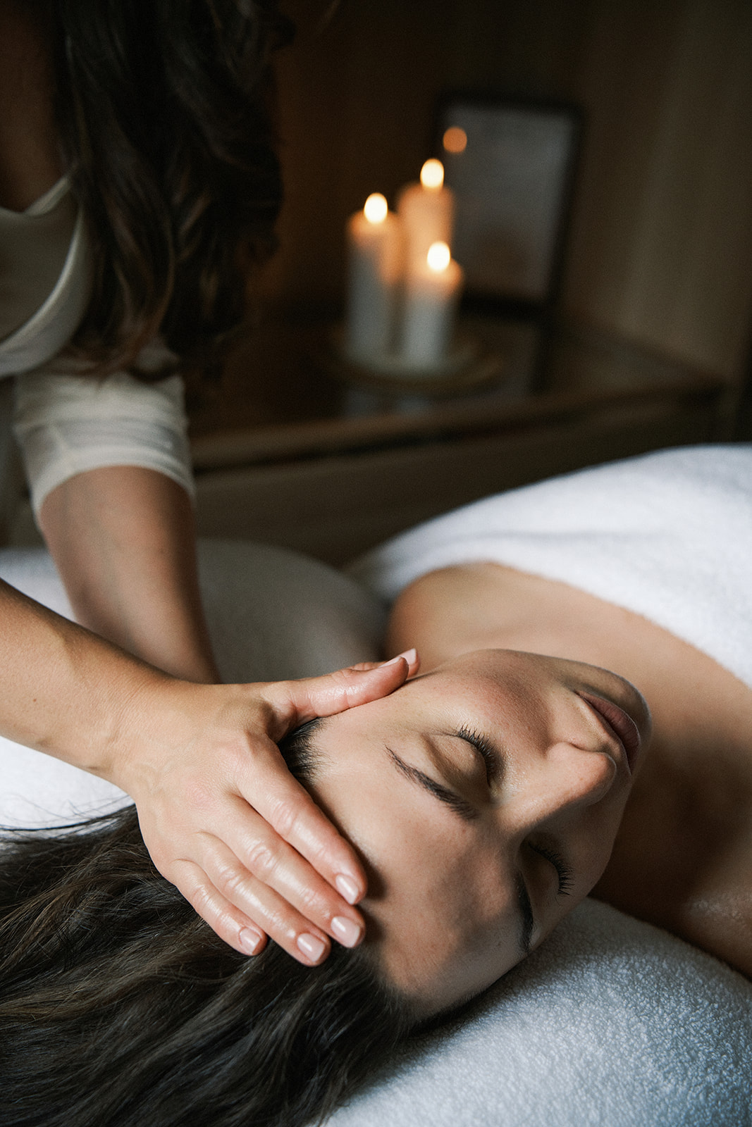 Gentle hands cradling a client's face during a restorative facial treatment in a softly candlelit room